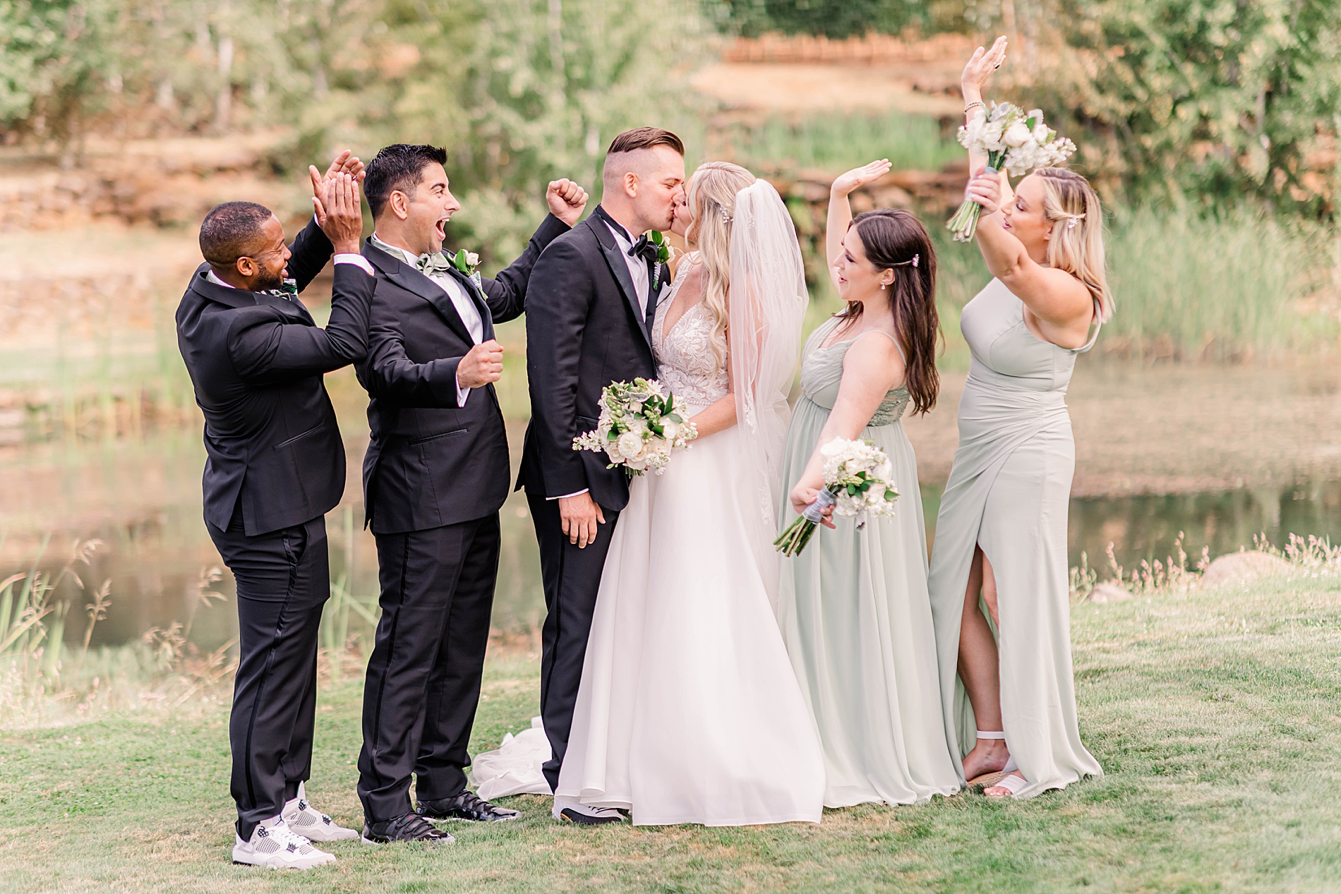 bride and groom kiss with their wedding party cheering them on
