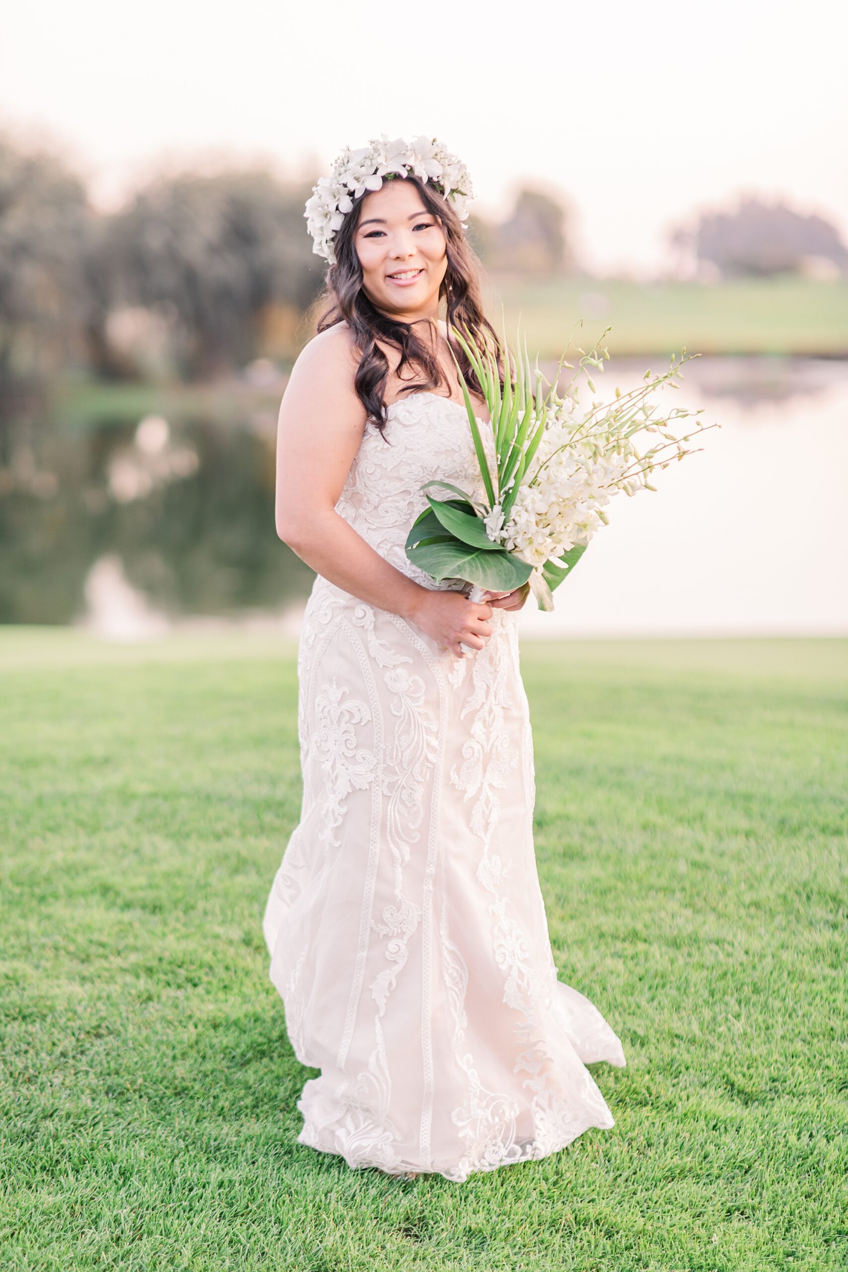 bride stands by pond holding white Hawaiian flower bouquet 